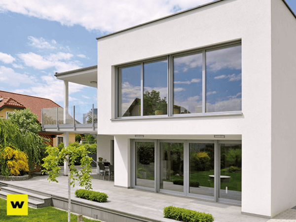 Modernes Einfamilienhaus mit großen Fenstern, Terrasse und gepflegtem Garten bei Sonnenschein.