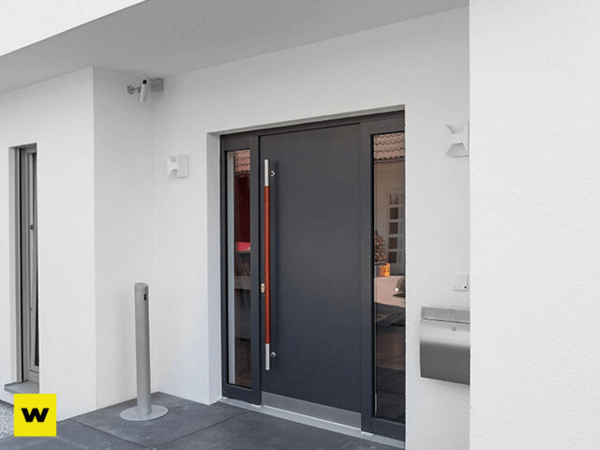 Moderne Haustür aus Aluminium mit Seitenteil, Glas und Edelstahlgriff an weißer Fassade.